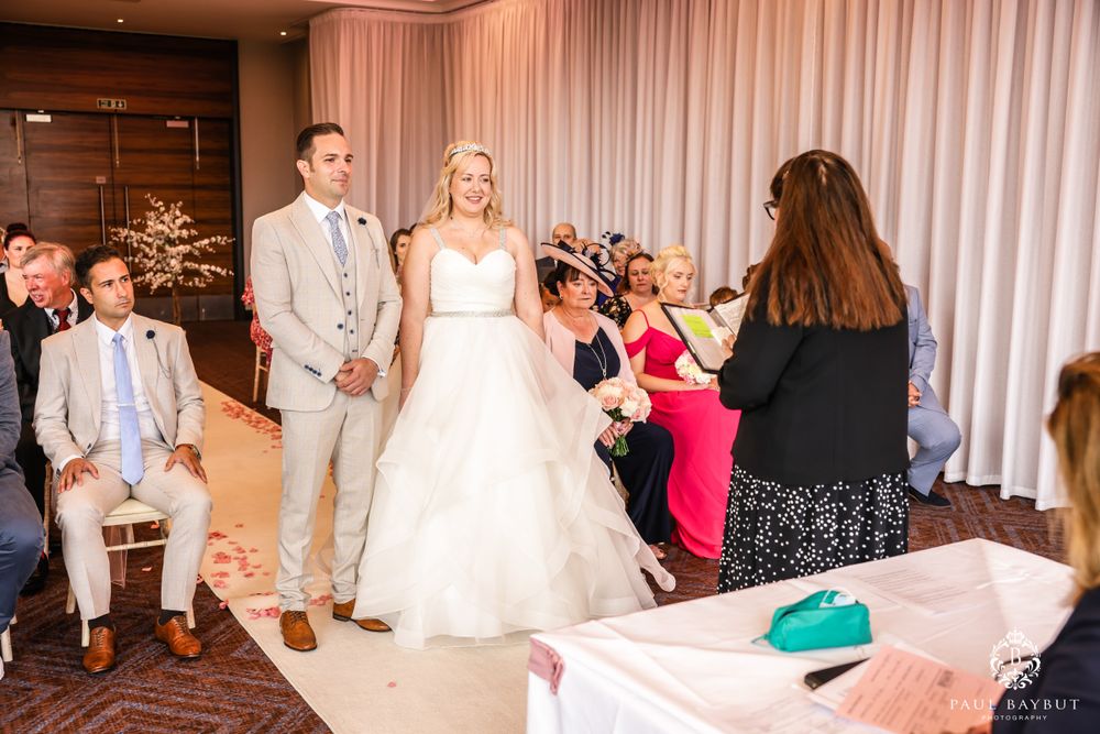 Wedding ceremony in progress with white aisle runner and pink accent lighting.
