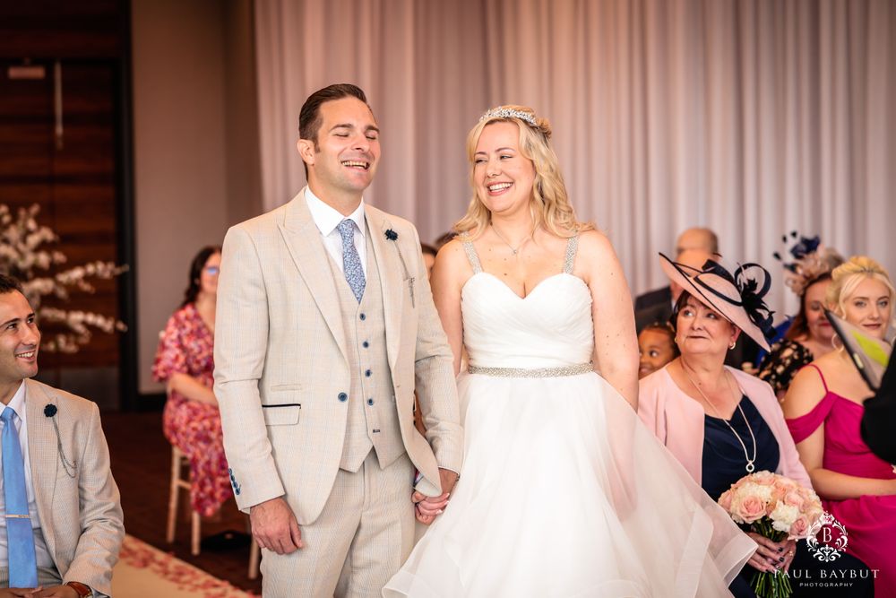 Couple shares a joyful moment during their wedding ceremony in an elegant indoor venue with beige curtains.