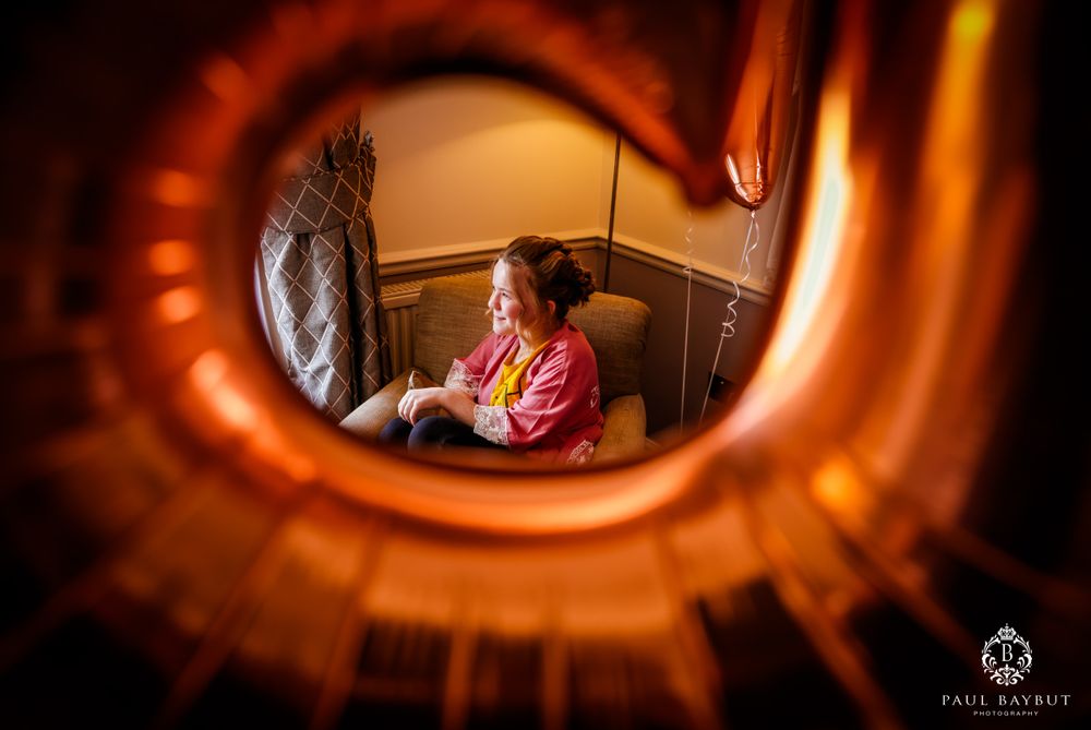 View through decorative mirror frame showing person in pink robe during wedding preparations.