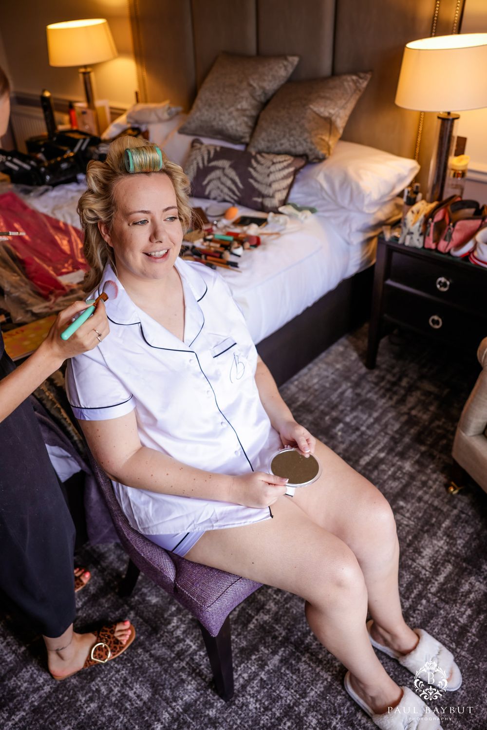 Wedding preparation scene in hotel room with person in white pajamas sitting on chair.