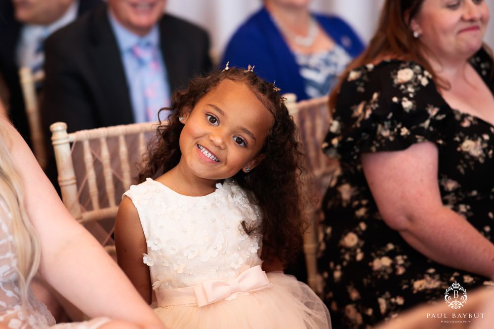 Young attendee in white dress and tiara smiles during wedding reception.
