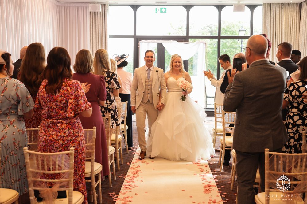 Wedding couple makes grand entrance down aisle with guests seated on both sides.