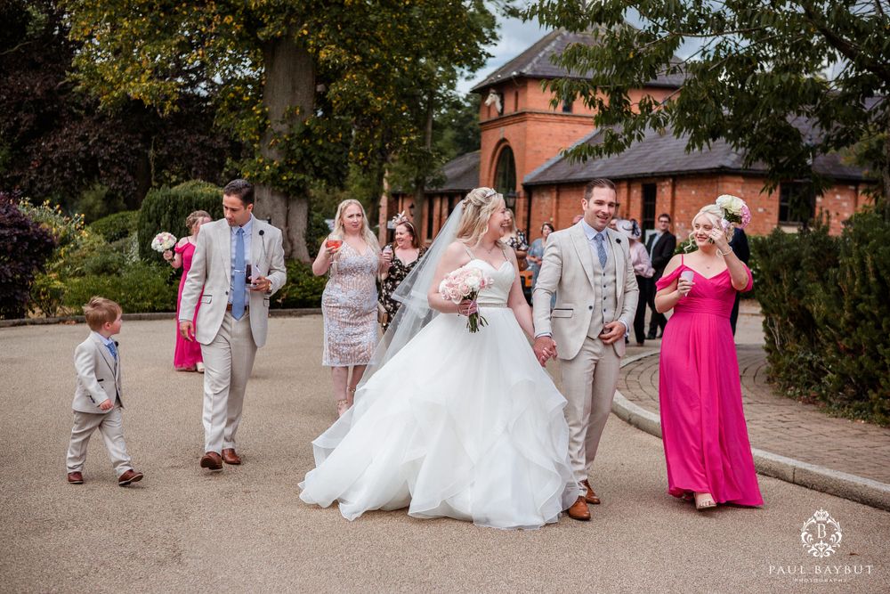 Wedding party walking outdoors with formal attire in white, pink and gray colors.