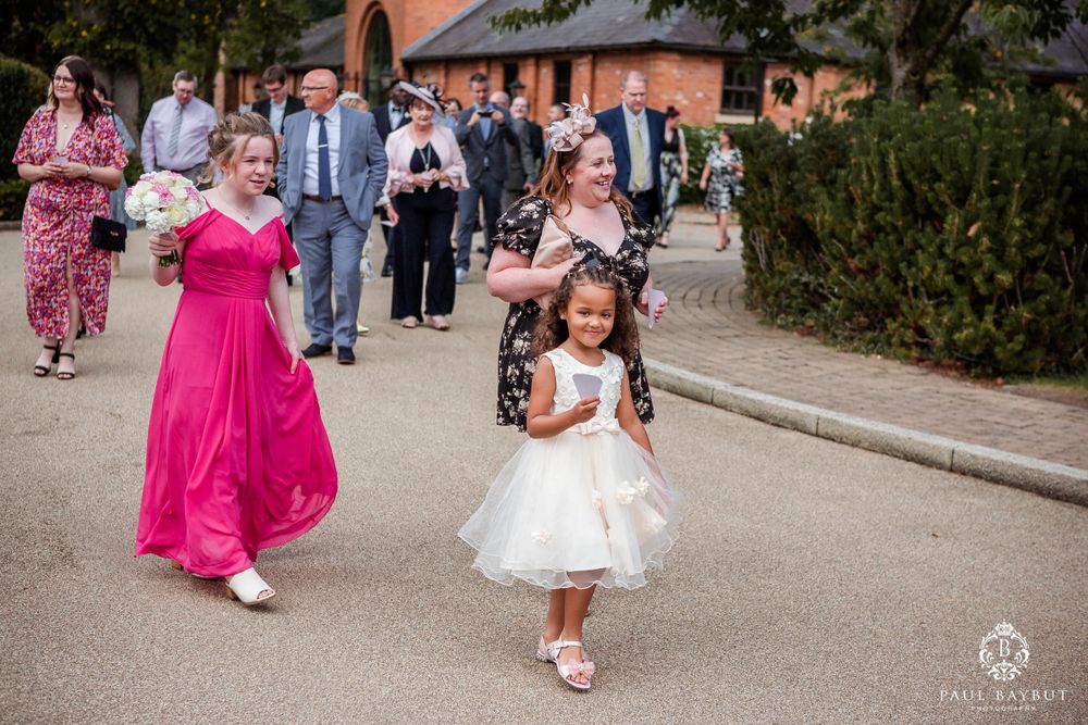 Wedding processional with bright pink dress and small flower girl in white walking along pathway.