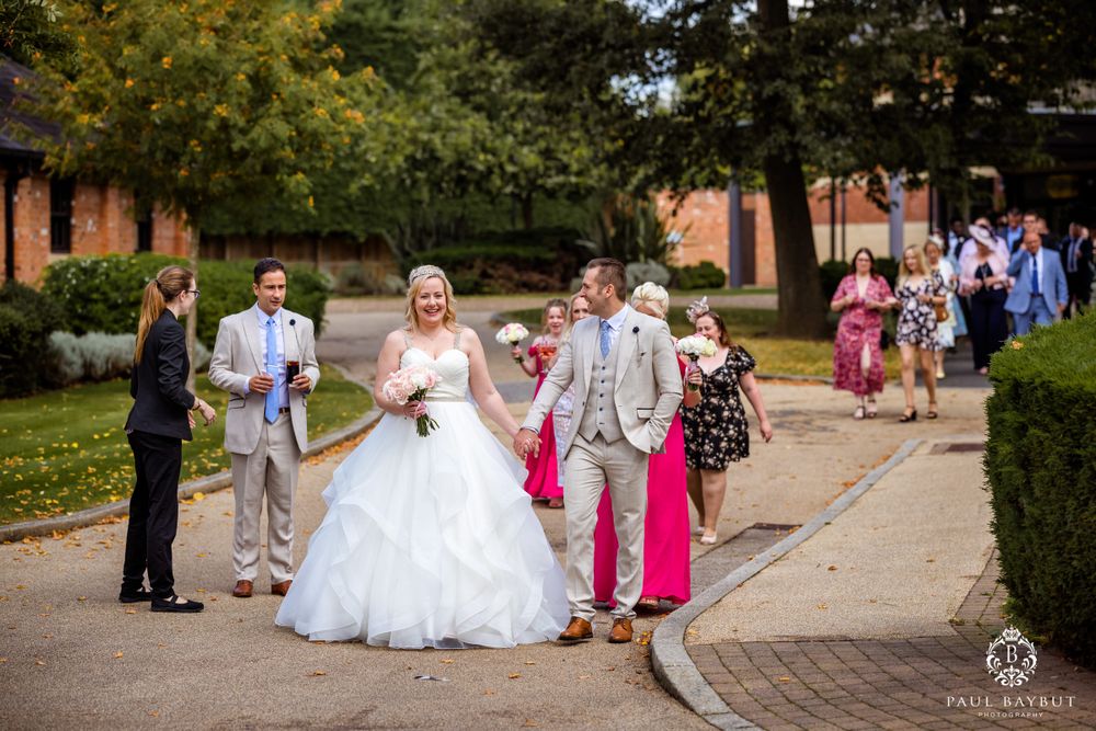 Wedding ceremony procession with white gown and light gray suits walking along brick building path.