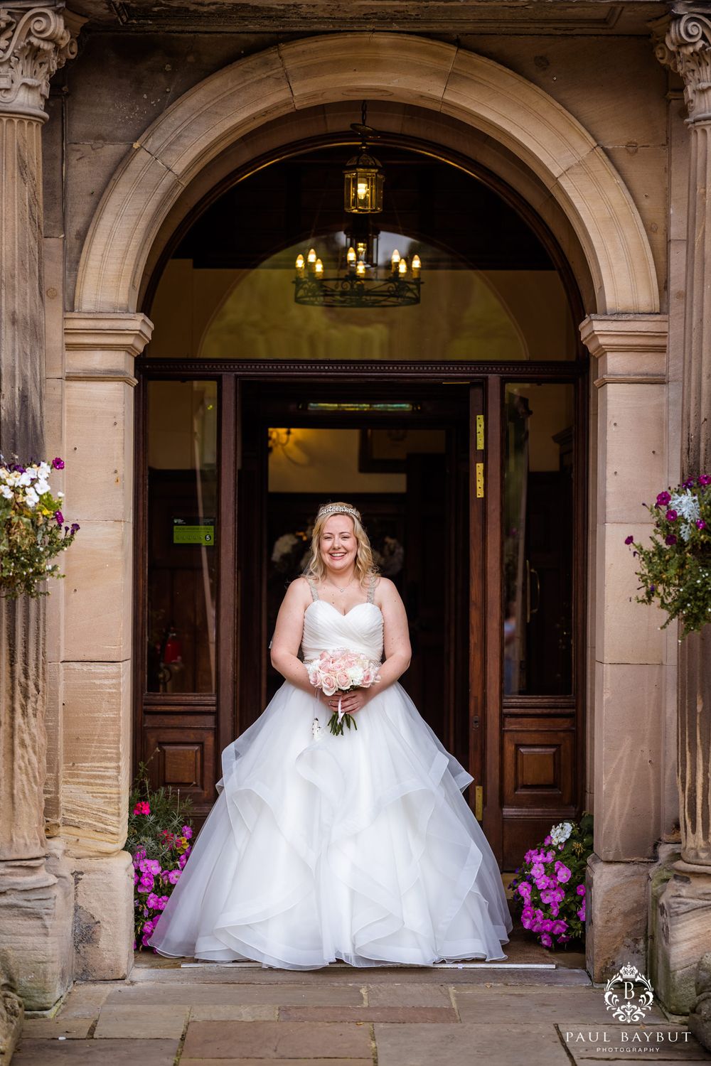 Elegant bridal portrait under stone archway with hanging flowers and chandelier.