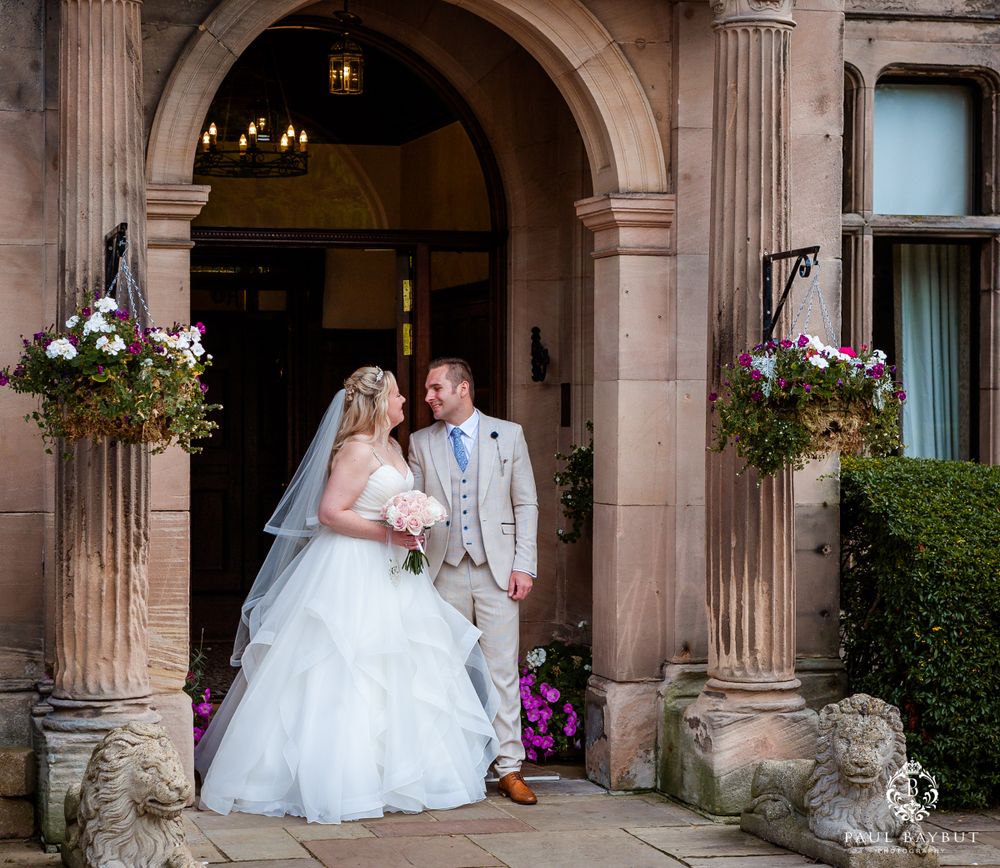 Romantic wedding portrait under ornate stone archway with decorative flowers.