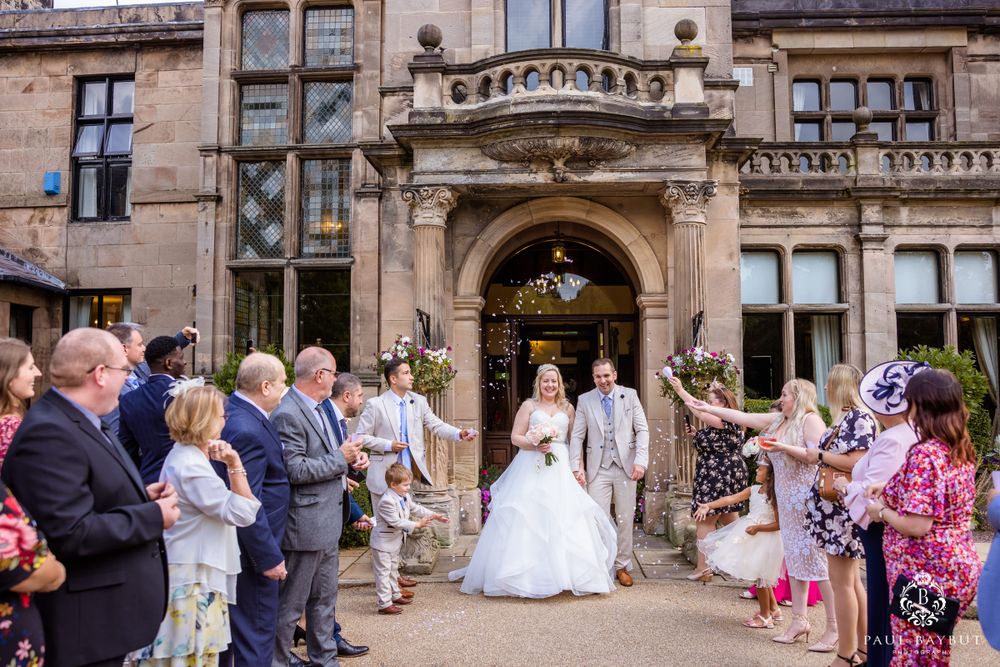 Guests celebrate as the wedding couple exits a historic stone building with ornate architecture.