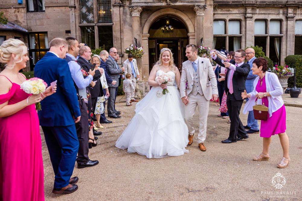 Wedding guests line up outside a historic venue to celebrate as the newlyweds walk through.
