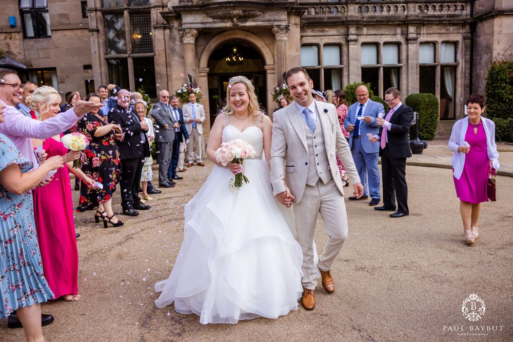 The happy couple walks through a line of wedding guests outside a grand stone building.