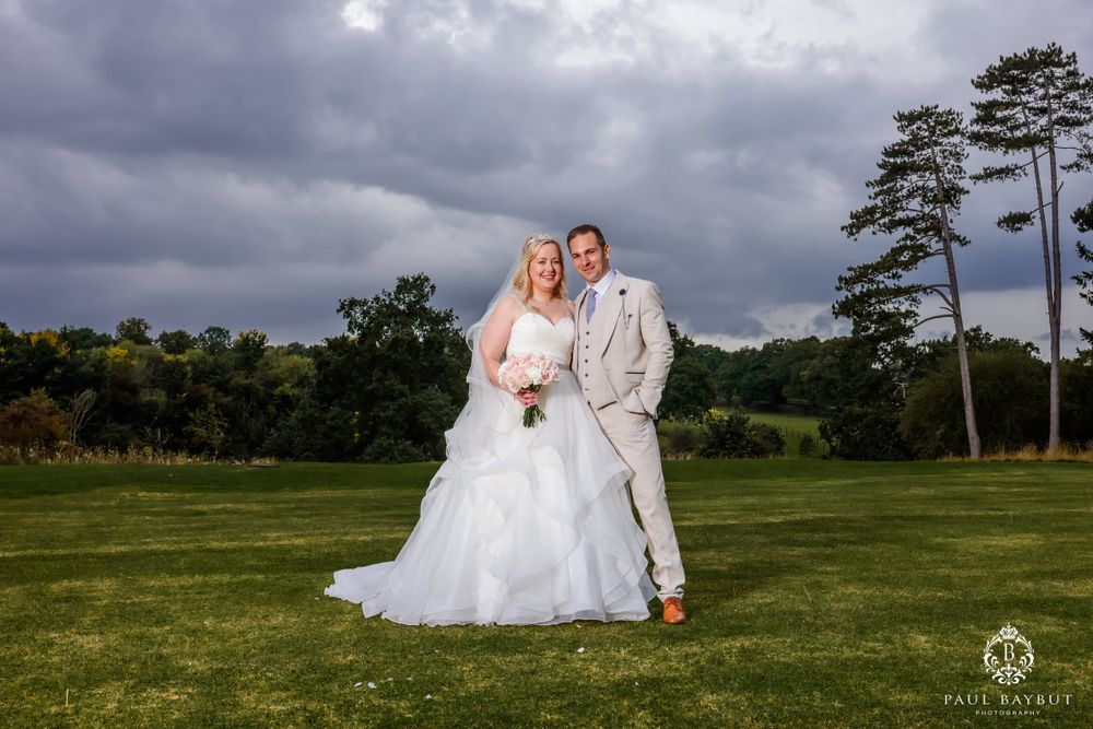 Newlyweds pose together on a golf course with dramatic stormy skies overhead.