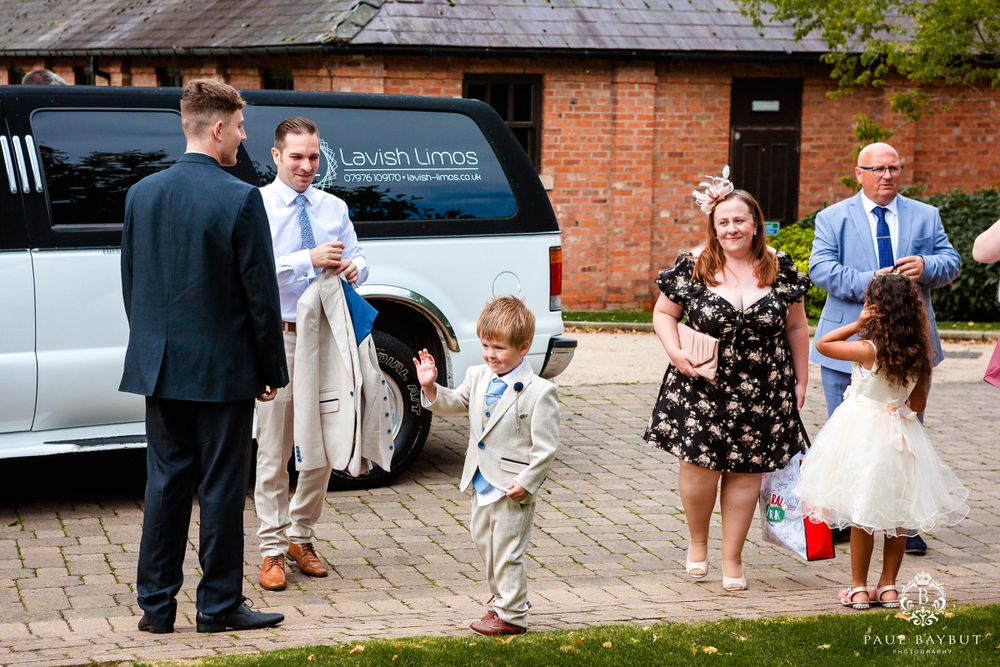 Group gathering outside by white limousine for wedding celebration.