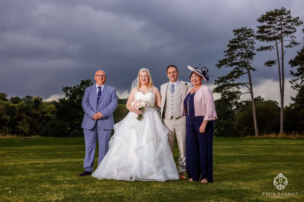 Family wedding portrait taken outdoors with dark stormy clouds and pine trees in background.