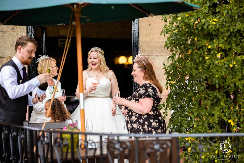 Wedding guests enjoying drinks on an outdoor terrace under a green umbrella.