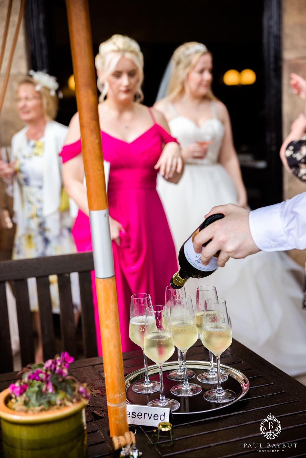 Champagne being poured into glasses on a tray at an outdoor wedding reception.