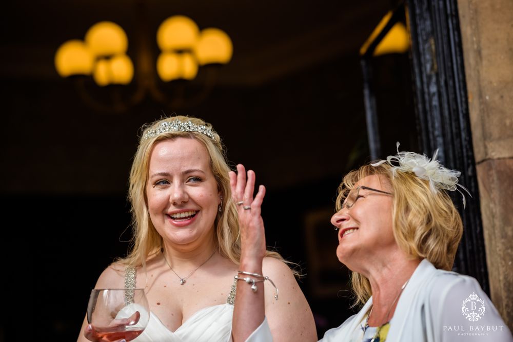 Two wedding guests share laughter and drinks during an outdoor celebration.