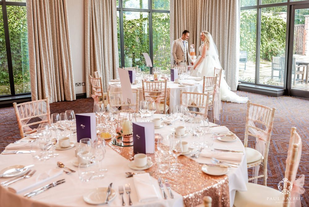 Elegant wedding reception tables set with sequined rose gold linens and white place settings in a bright venue.