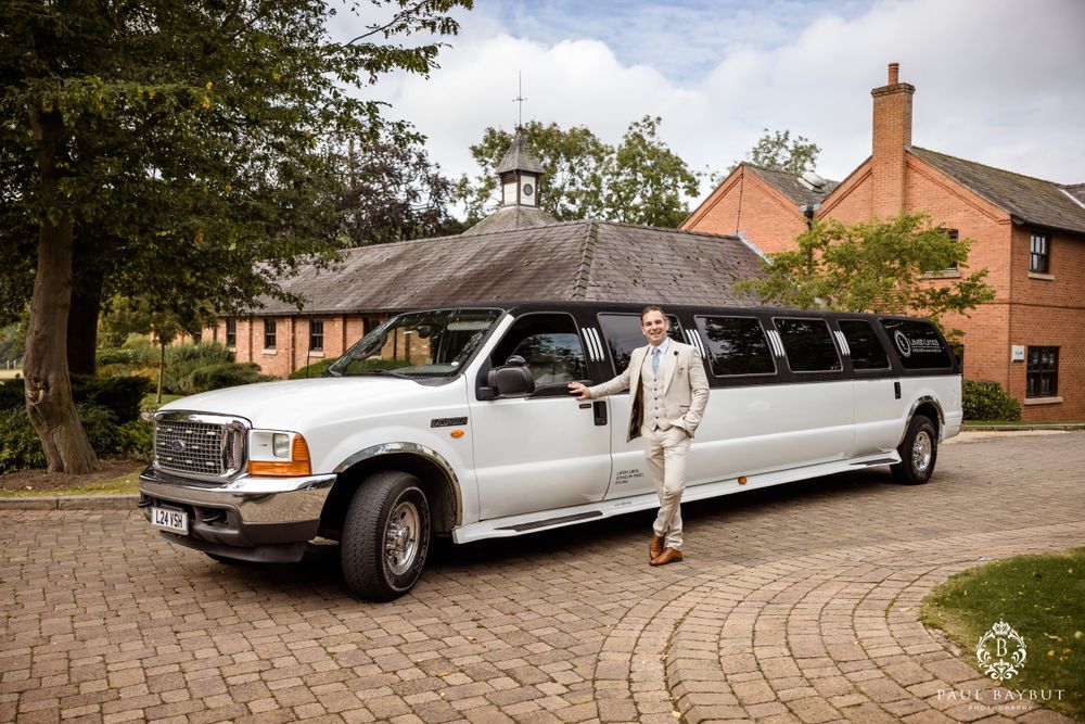 White stretch limousine parked on brick driveway with person standing beside it.