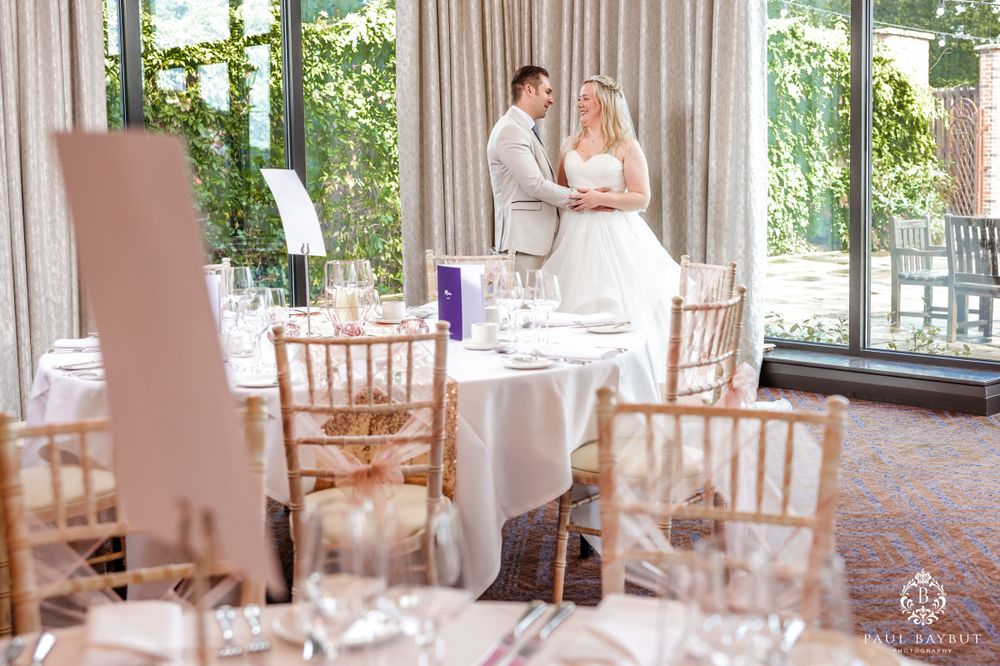 Wedding reception setup showing tables with rose gold decor and floor to ceiling windows.