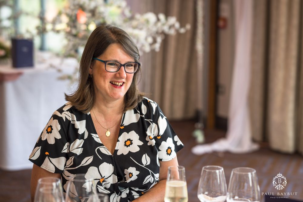 Guest smiling at wedding reception wearing floral print dress and glasses.