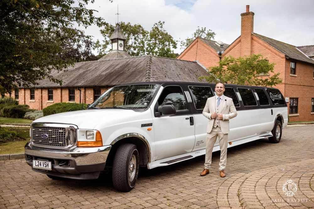 White stretch Ford limousine parked outside brick building with person posing next to it.