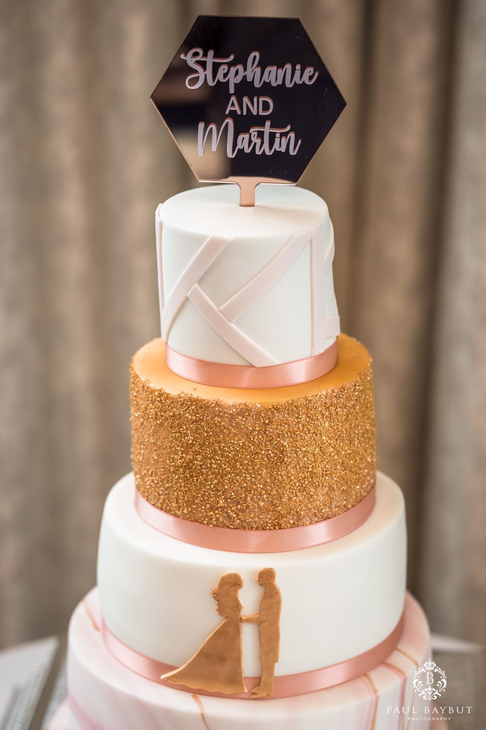 Three-tier wedding cake with rose gold accents featuring modern geometric topper.