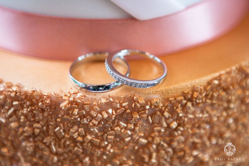 Two silver wedding rings with diamonds rest on a peach and gold textured surface.