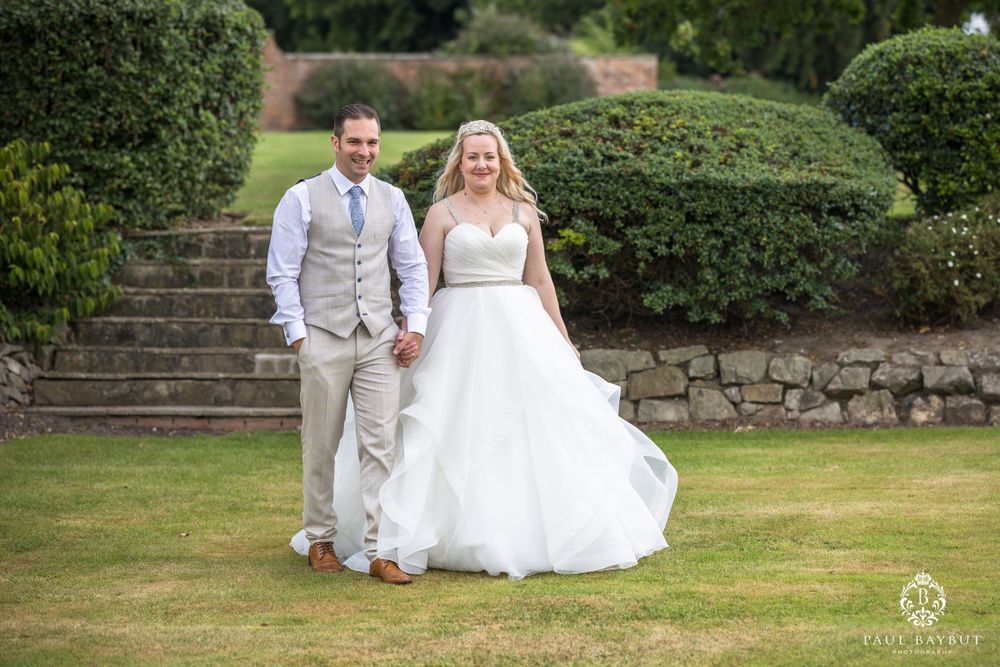 A couple descends stone garden steps on their wedding day surrounded by manicured hedges.