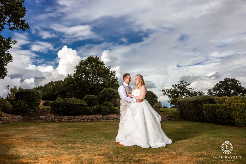 A wedding couple poses in a garden setting against dramatic cloudy blue sky.