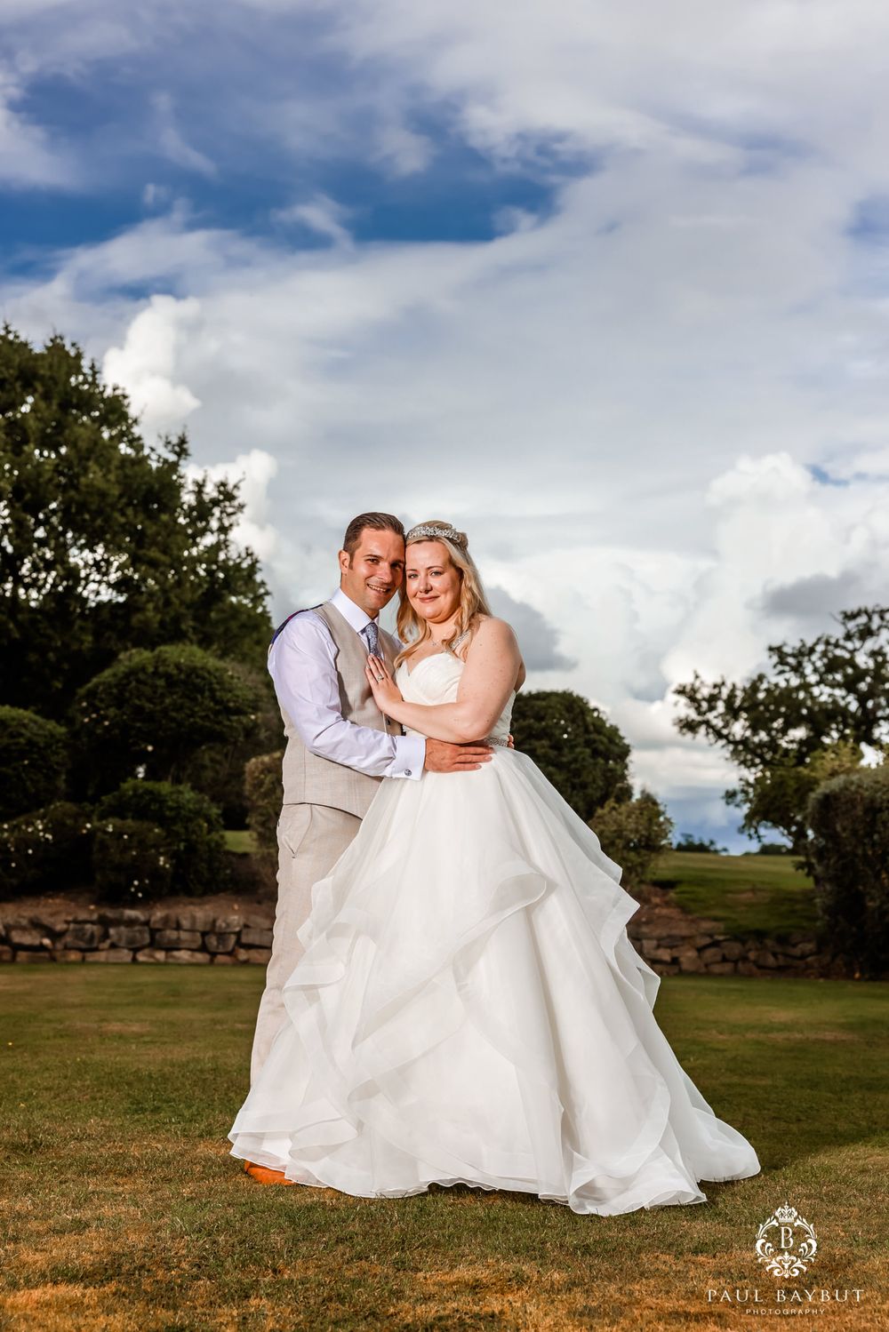 A wedding portrait captured in a landscaped garden with dramatic clouds in the background.