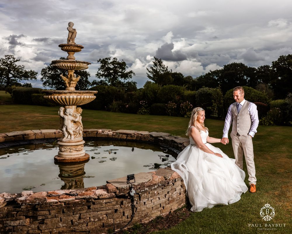 Wedding photo at dusk featuring elaborate tiered fountain with couple by stone basin.
