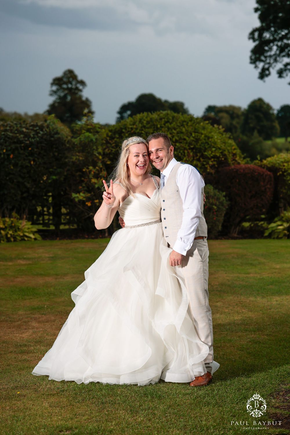 Joyful wedding portrait on manicured lawn with hedges and gardens in background.