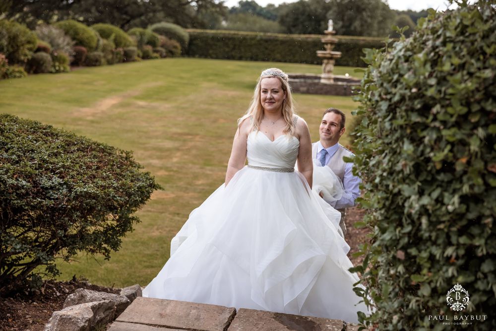 Wedding moment captured on garden path with fountain visible in distance.