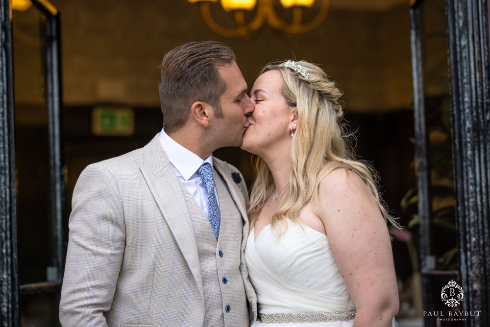 A romantic wedding kiss between newlyweds, with the bride in white and groom in light gray suit and blue tie.