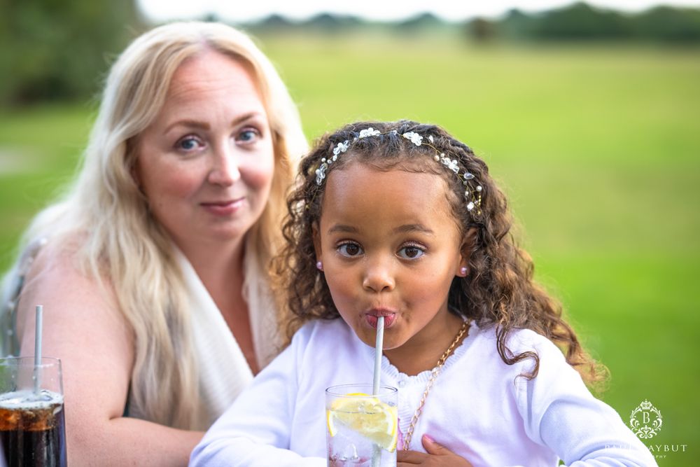 A child sips a drink through a straw while sitting outdoors at a wedding reception.