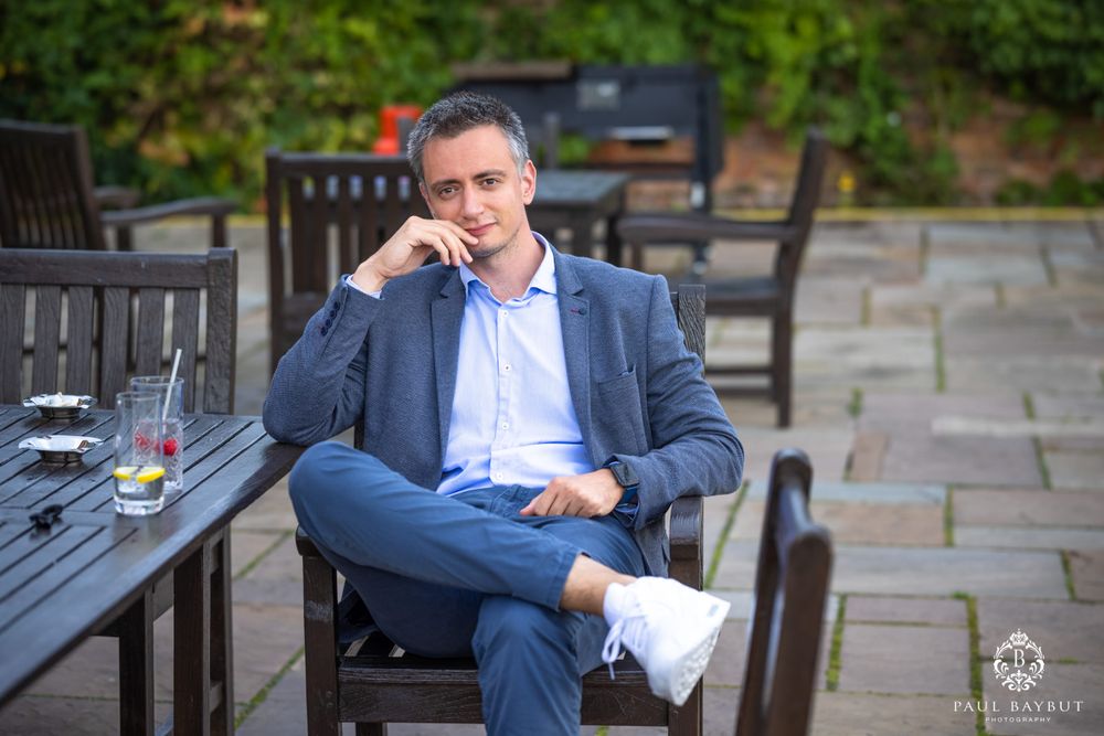 A guest in a navy suit relaxes at an outdoor table with drinks.