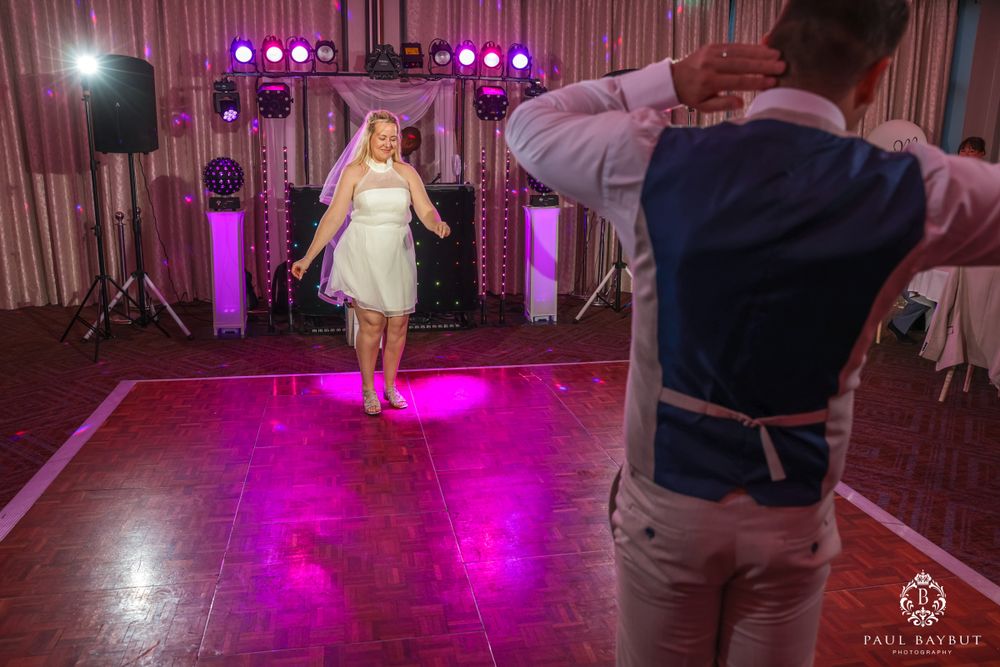 A photographer captures a bride dancing on a purple-lit dance floor.