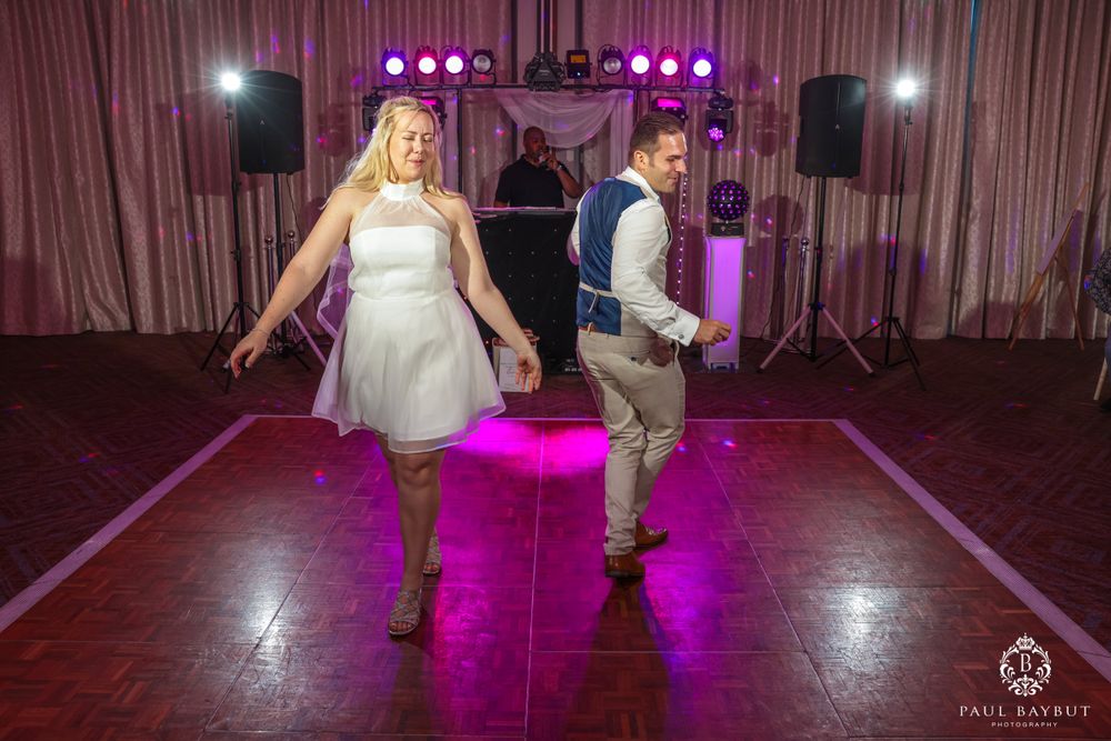 Two people dancing energetically on a hardwood floor with purple lighting and stage equipment.
