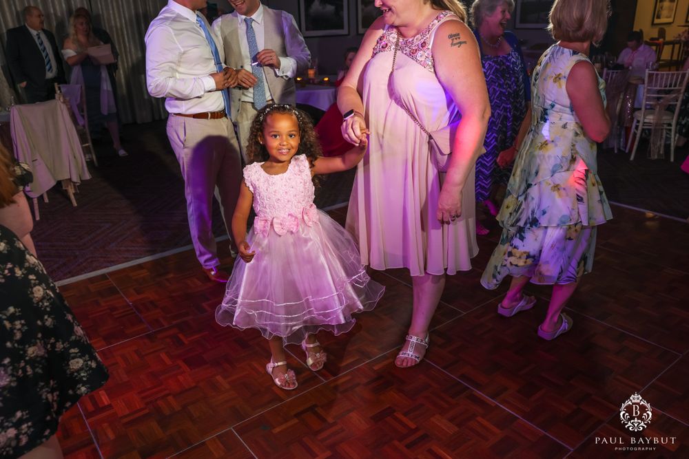 A young child in a purple tulle dress dances on a wooden floor under pink lighting.