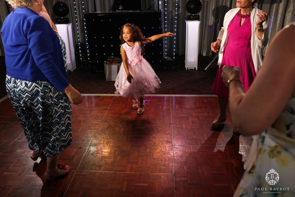 A child in a pink dress jumps excitedly while dancing on a wooden floor.