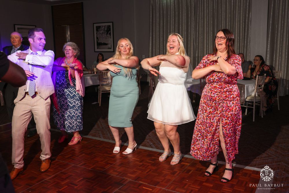 Wedding party performing a choreographed line dance on a wooden dance floor.