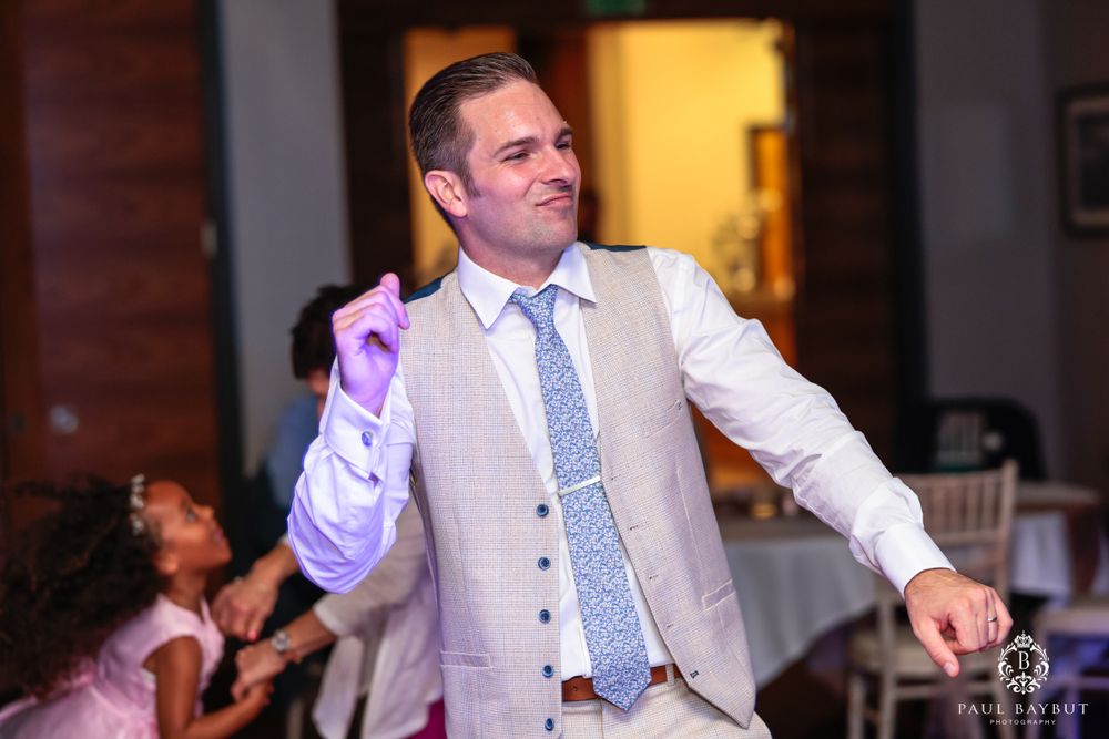 Guest in light suit and tie dancing enthusiastically at a wedding reception.