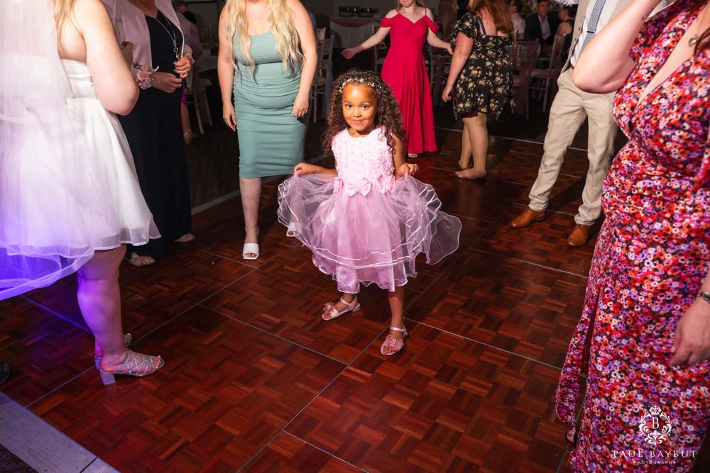 Young guest in pink tulle dress twirling on the dance floor during wedding reception.
