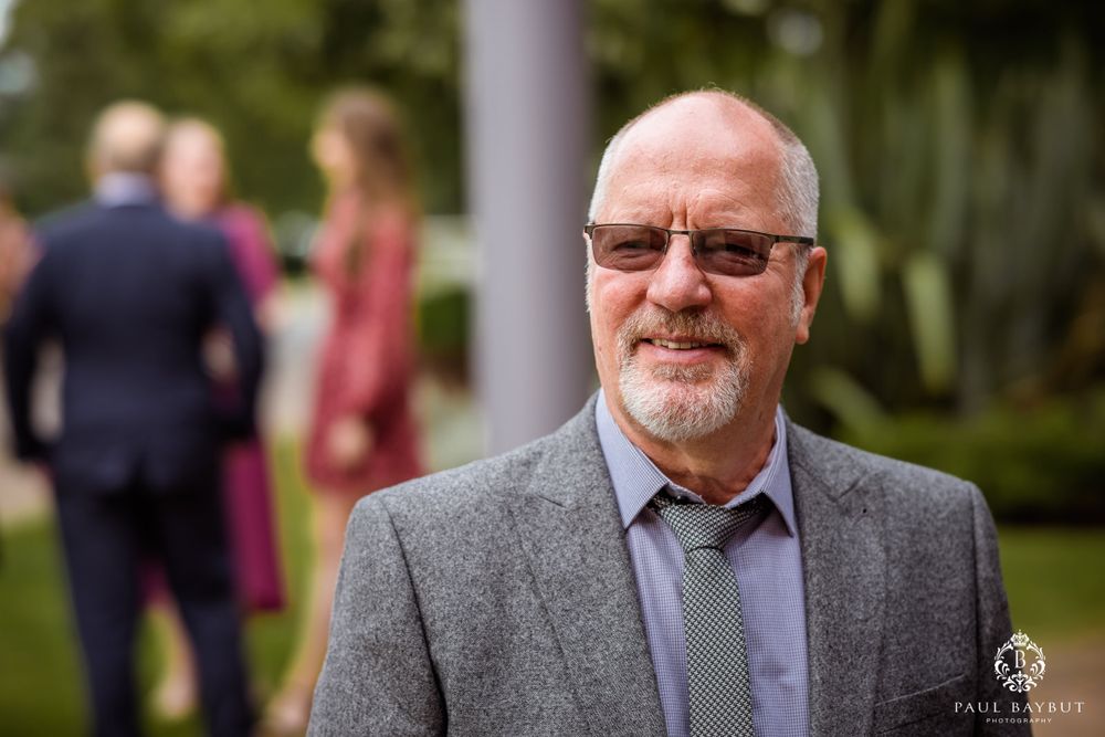 Person in gray suit with glasses standing outdoors at formal event.