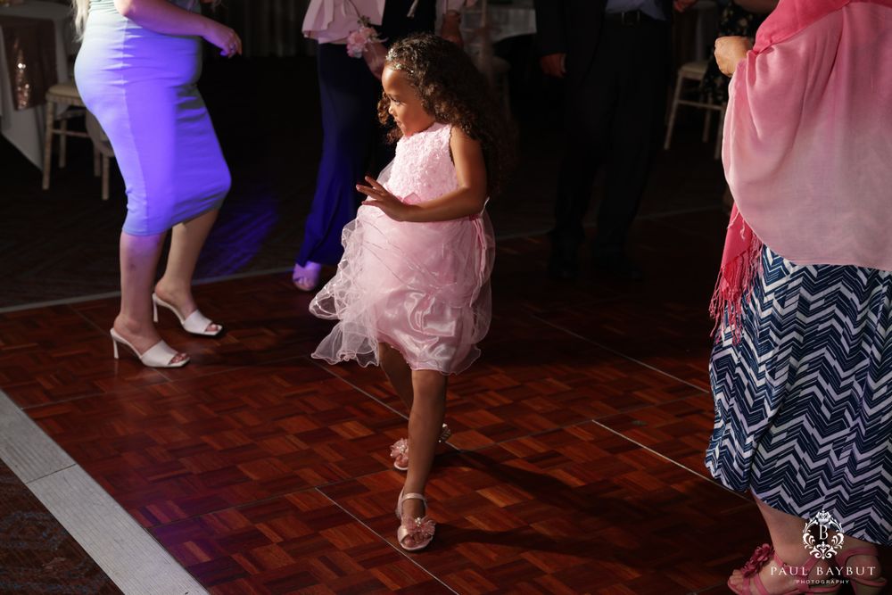 Child in pink dress dancing playfully on wooden dance floor during celebration.