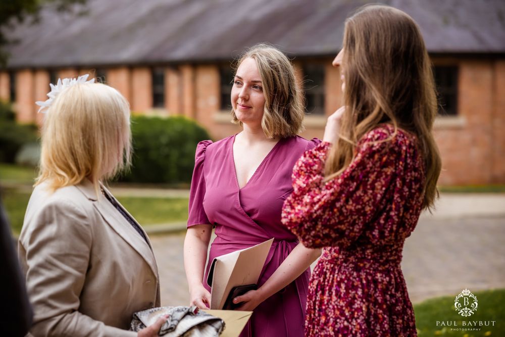 Wedding planners in pink and floral dresses discuss details outside a brick venue.