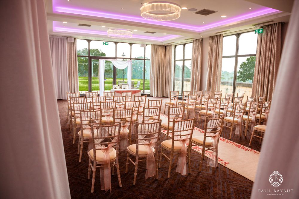 Wedding venue interior with rows of gold chiavari chairs and purple ambient lighting.
