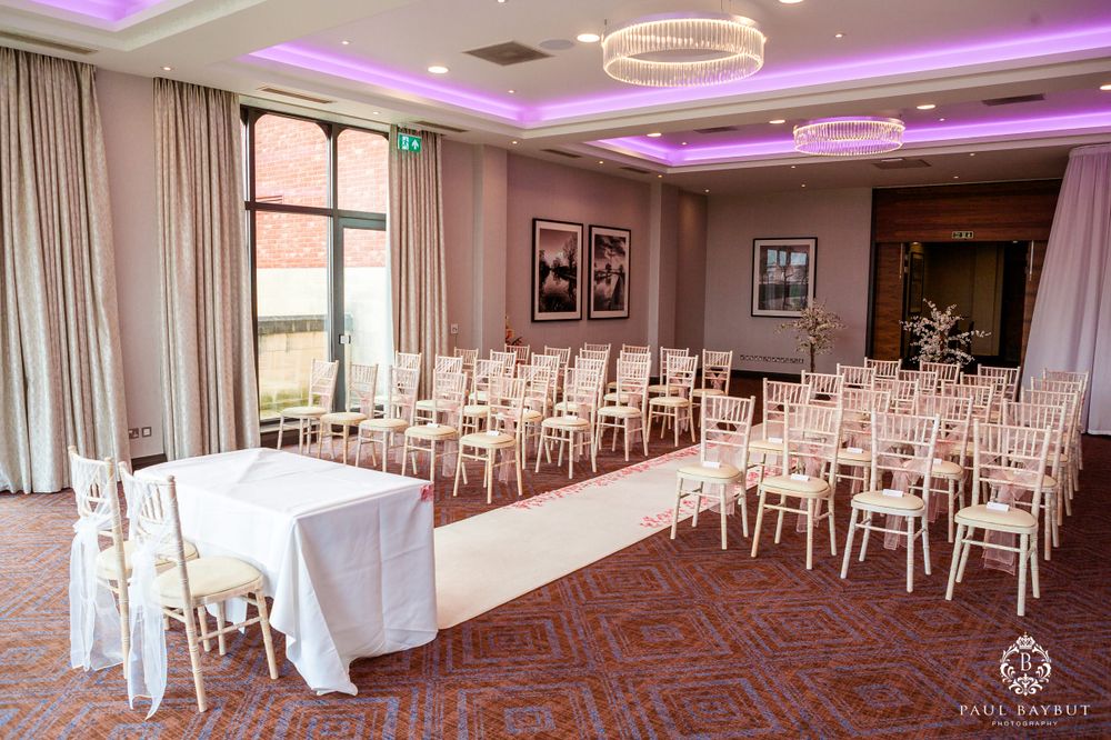 Wedding ceremony room with white chairs and purple ceiling lighting features circular chandeliers.