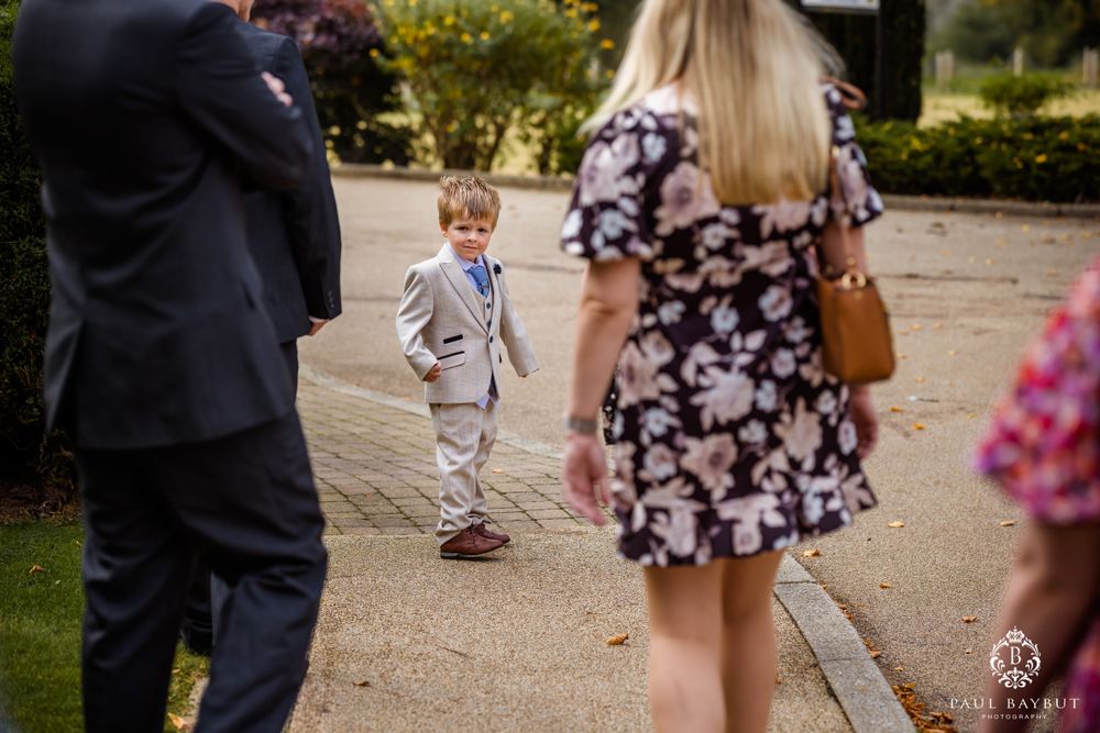Young ring bearer in light suit poses during outdoor wedding celebration.