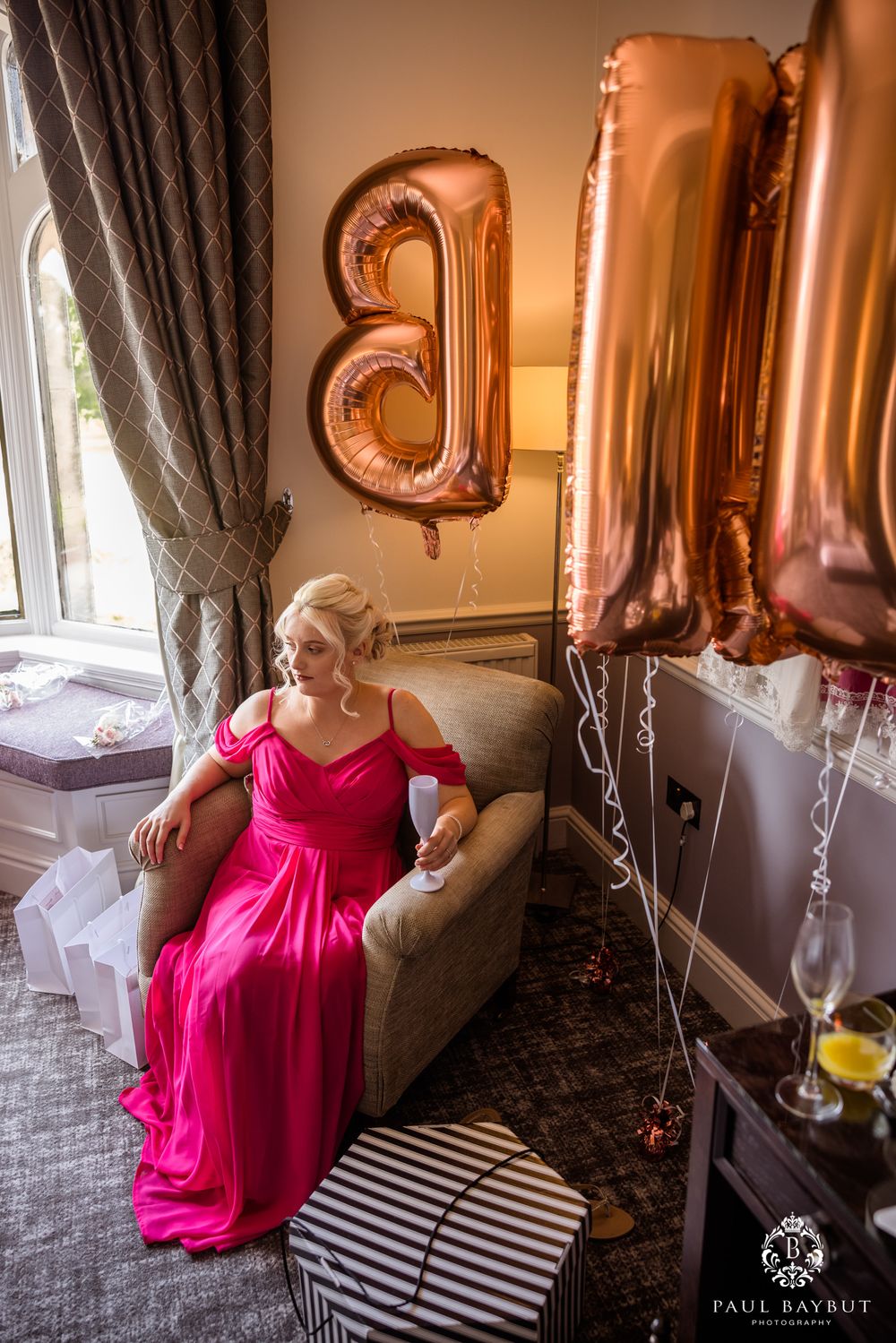 Pink ballroom setting with rose gold number balloons and elegant curtains.